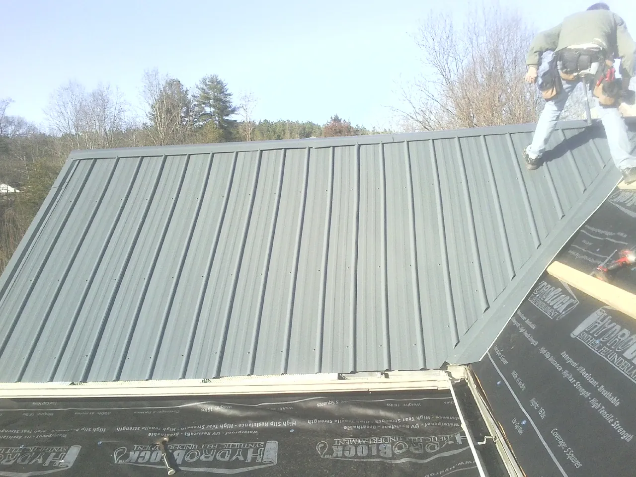 Crew installing dark green standing seam panels over synthetic underlayment in Terre Hill