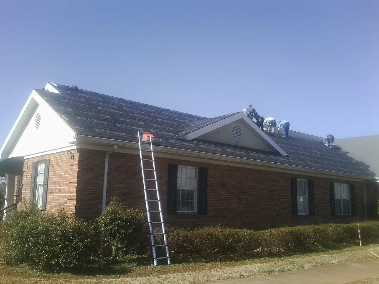 Crew tearing shingles off a brick ranch roof with a ladder set — Metal Roof Repair work by our crew in Terre Hill