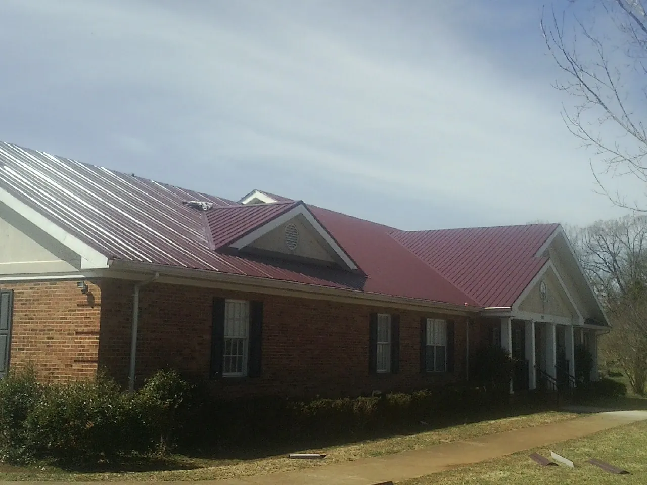Red metal roof with gabled entries on a long brick building, from a Hail Damage Roof Repair job in Terre Hill