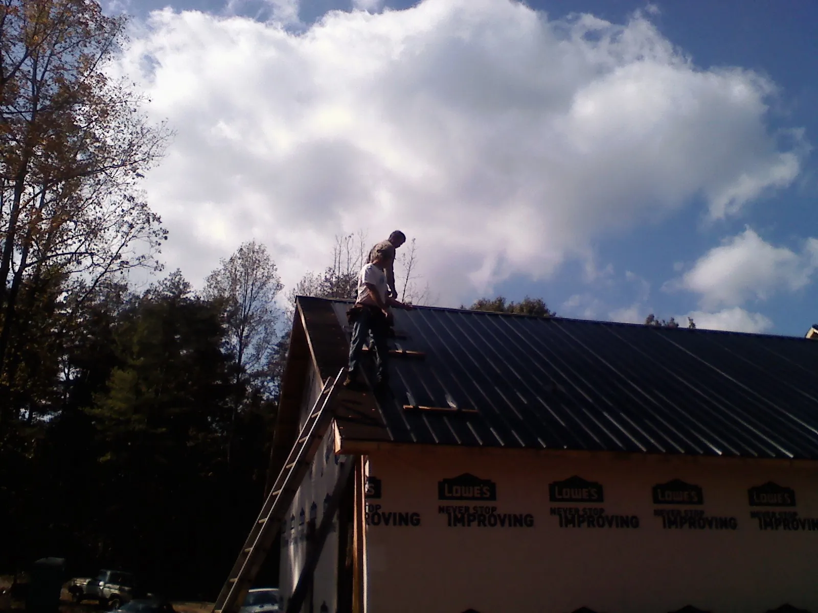 Roofer fastening dark metal panels high against a cloudy sky, from a Roof Inspection job in Terre Hill