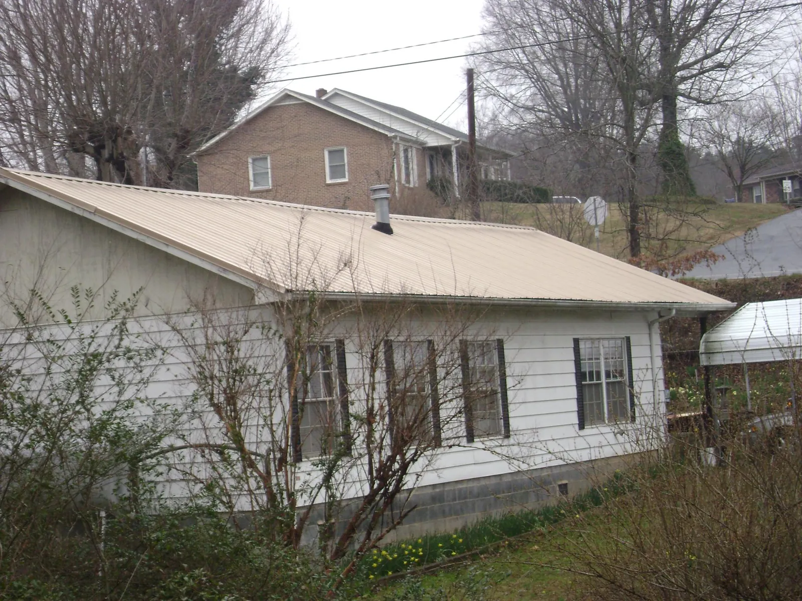 Tan metal roof on a white sided house set into a hillside — Commercial Roofing by Roofing Brothers in Terre Hill
